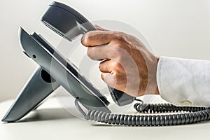 Male hand picking up the receiver of a telephone