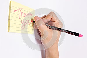 Male Hand with Pink Fluorescent Marker Writing Thank You Word in Yellow Sticky Notebook with Line