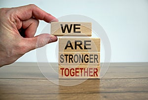 Male hand placing a block with word `we` on top of a blocks tower with words `are stronger together`. Wooden table. Beautiful