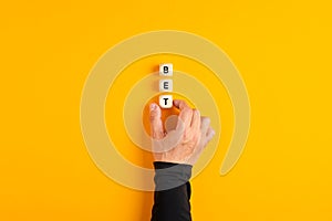 Male hand placing the wooden blocks with the word Bet on yellow background