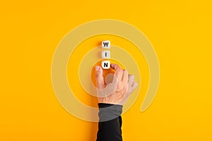 Male hand placing the wooden blocks with the word win on yellow background. Winning strategy in business or competition