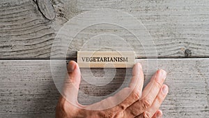 Placing wooden peg with a Vegetarianism sign on it over white wooden background photo