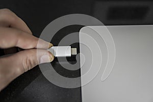 Male hand plugging white USB-C Type C cable into a port on a grey laptop notebook computer. USB type-C port and Cable`s