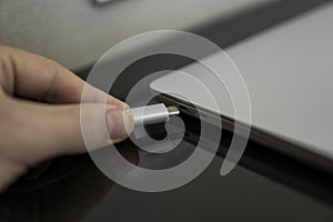 Male hand plugging white USB-C Type C cable into a port on a grey laptop notebook computer. USB type-C port and Cable`s
