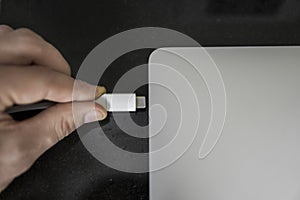 Male hand plugging white USB-C Type C cable into a port on a grey laptop notebook computer. USB type-C port and Cable`s