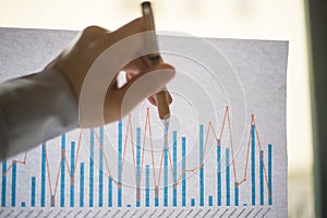 Male hand pointing at a coloured column chart printed on a white sheet of paper during a business meeting