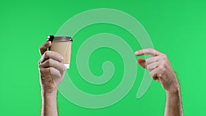 The male hand points with the index finger to the other hand holding a paper cup of coffee and shows the thumb up. Close