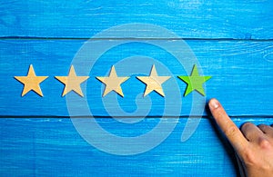 The male hand points to the fifth green star on a blue wooden background. Five Stars. Rating of restaurant or hotel, application.