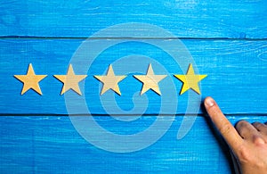 The male hand points to the fifth yellow star on a blue wooden background. Five Stars. Rating of restaurant or hotel, application.