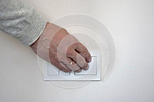 Male hand presses button of white switch mounted on light wall. Close-up
