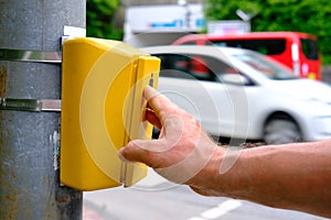 Male hand presses a yellow device with a button on demand with a symbol of a man to cross the road, a pedestrian observes the