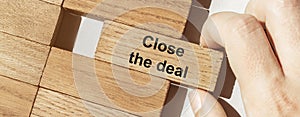 Male hand pushes a piece of wood with text Close the deal from other pieces of wood