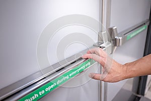 Male hand pushing panic bar on emergency fire exit door