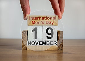 Male hand puts a block with the inscription `International Mens Day` on cubes with the date November 19. Wooden table. Beautiful