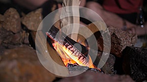 Male hand putting firewood into campfire