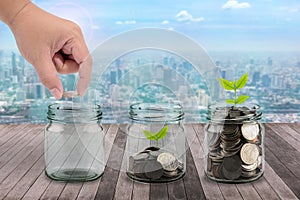 Male hand putting money coins in clear bottle and little tree on