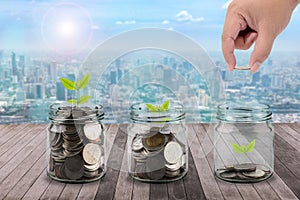 Male hand putting money coins in clear bottle and little tree on