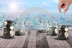 Male hand putting money coins in clear bottle on wooden Plank co