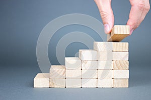 Male hand putting wooden blocks in the form of a ladder. The concept of building a success