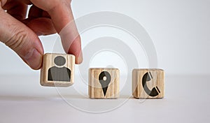 Male hand putting wooden cube with human icon near other cubes with geoposition and phone marks, contact and information icons
