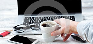 Male hand reaching for a cup of coffee with workstation technology in background