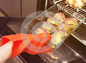 Male hand in a red silicone glove tack puts a glass tray with stuffed champignons in the oven