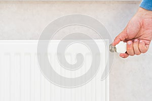 Male hand regulates the thermostat knob on the white heating radiator with at home a cold season.