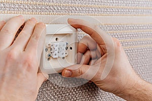 male hand replaces or repairs the light switch on the wall with brown wallpaper.