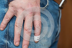 Male hand rests on his thigh. Middle-aged man is wearing blue jeans with brown leather belt. Index finger is wrapped in white tape