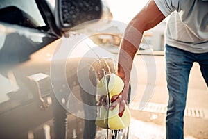 Male hand rubbing the car with foam, carwash