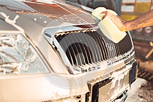 Male hand rubbing the car with foam, carwash