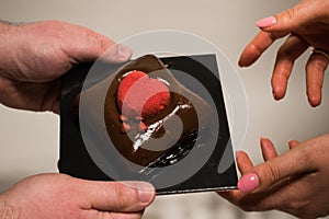Male hand`s holding and offering a choco pastry cake to woman`s hands