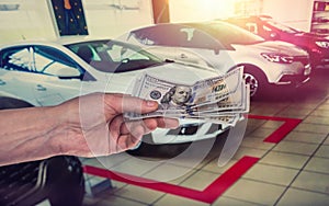 Male hand showing a dollar for buying a car in the autohouse