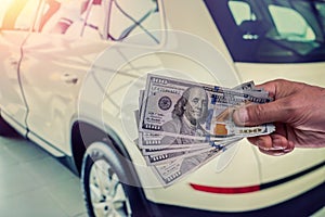 Male hand showing a dollar for buying a car in the autohouse
