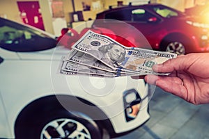 Male hand showing a dollar for buying a car in the autohouse