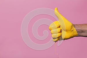 Male hand showing sign thumb up with paint flowing down on a colored background. creative idea, creative concept, gesture