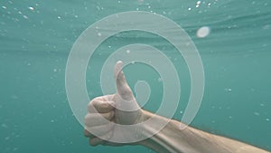 Male hand showing thumb up sign gesture on blue underwater background with bubbles. Gestures and signs. Body language on