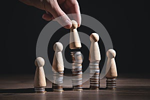 Male hand showing wooden human figure on coins stack