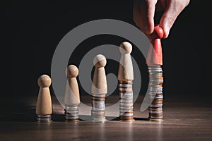 Male hand showing wooden human figure on coins stack