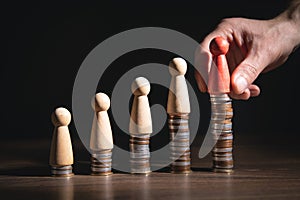 Male hand showing wooden human figure on coins stack