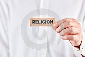 Male hand shows a wooden block with the word religion