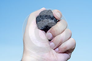 Male hand with a small piece of coal on a sky blue background