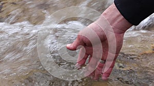 Male hand splashing in clean water flowing speedily in nature