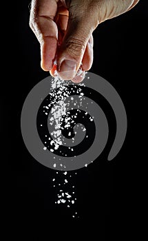 Male hand sprinkling edible salt at black background