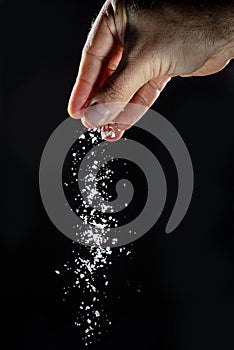 Male hand sprinkling edible salt at black background