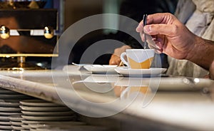 A male hand stirring an espresso coffee cup sitting in a bar counter in Italy, indoors