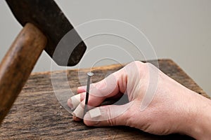 Male hand with stitches on fingers fixing the nail on the wood and hitting it with a hammer