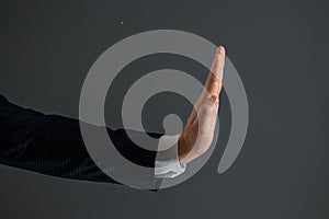 Male hand in a suit shows the palm of the stop gesture on a gray background. Stop concept, close-up