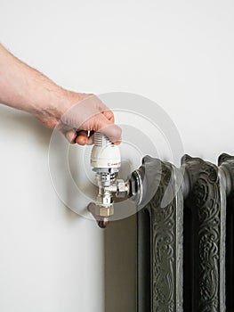 male hand switches the temperature on the radiator in the room