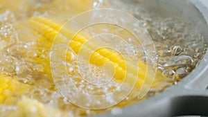 Male hand takes a glass lid from the pan in which sweet corn is boiling